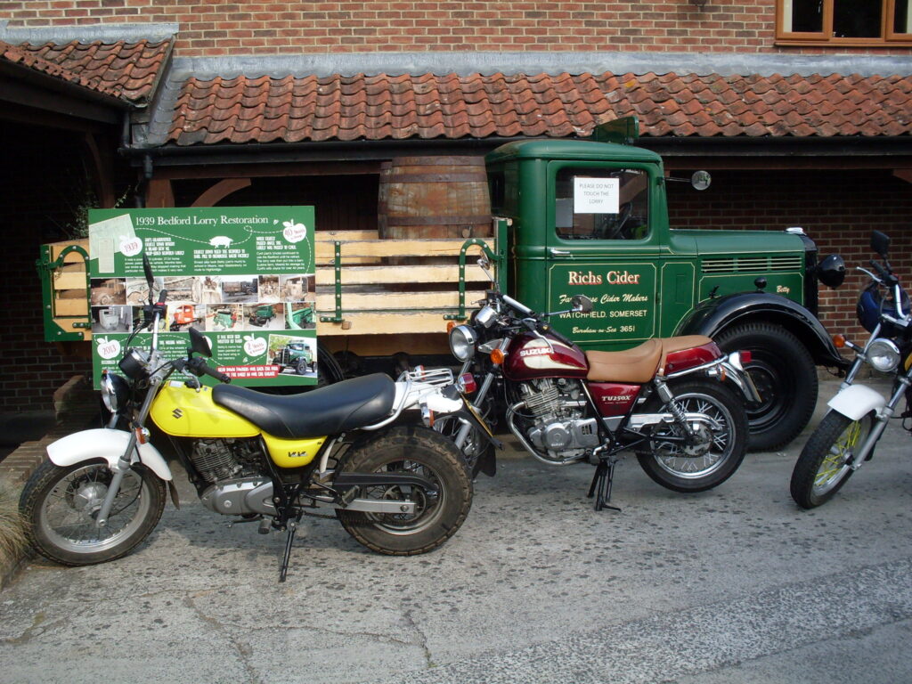 Two motorcycles in front of a 1940s Bedford lorry with placards telling of its restoration.