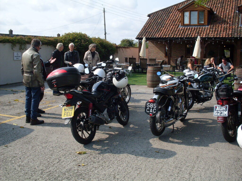 Motorbikes parked in the sun with onlookers enjoying the occasion.