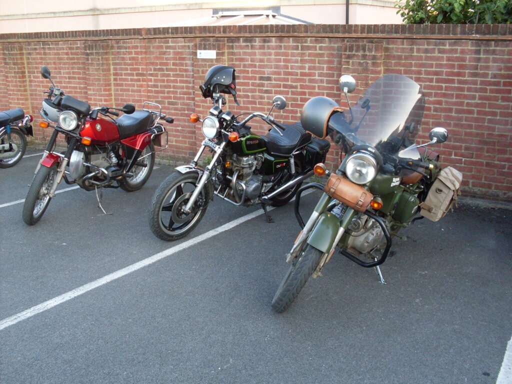 A red BMW airhead R80ST, a black (with green lining) Honda twin with high-bars and small leather panniers and a single-cylinder Royal Enfield in military style (green paint and canvas panniers) fitted with a substantial modern Givi windscreen.