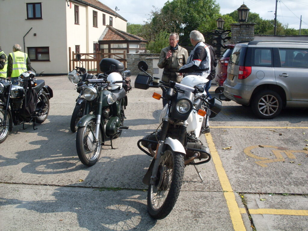 Motorbikes parked in the sun with onlookers enjoying the occasion.