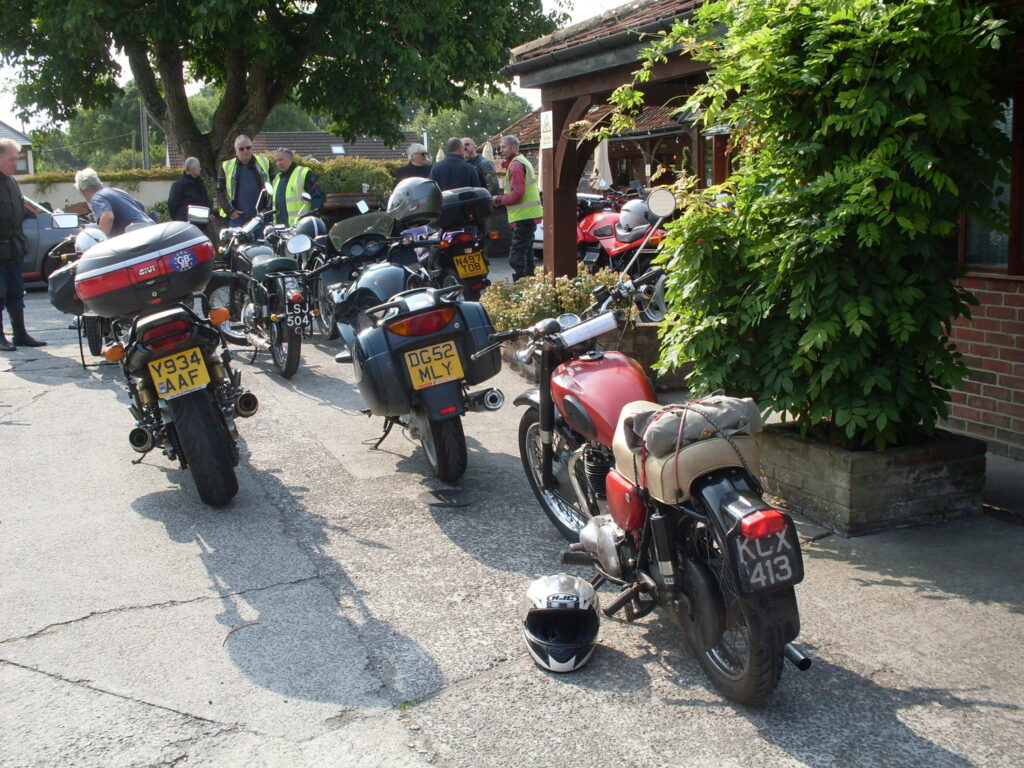Motorbikes parked in the sun with onlookers enjoying the occasion.