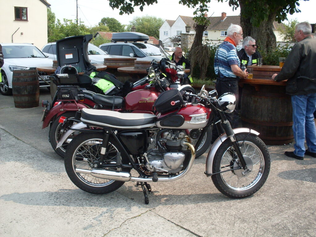 Three bikes (Triumph twin, Moto Guzzi Single and Honda) lined up one behind the other, each one with a red petrol tank.