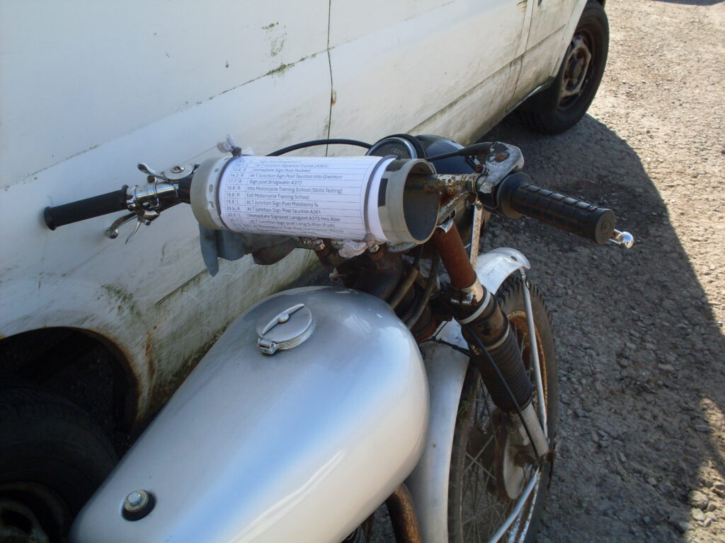 Looking down on the front of a bike with a piece of very large diameter pipe strapped to the handlebars and a route sheet wrapped around the pipe.
