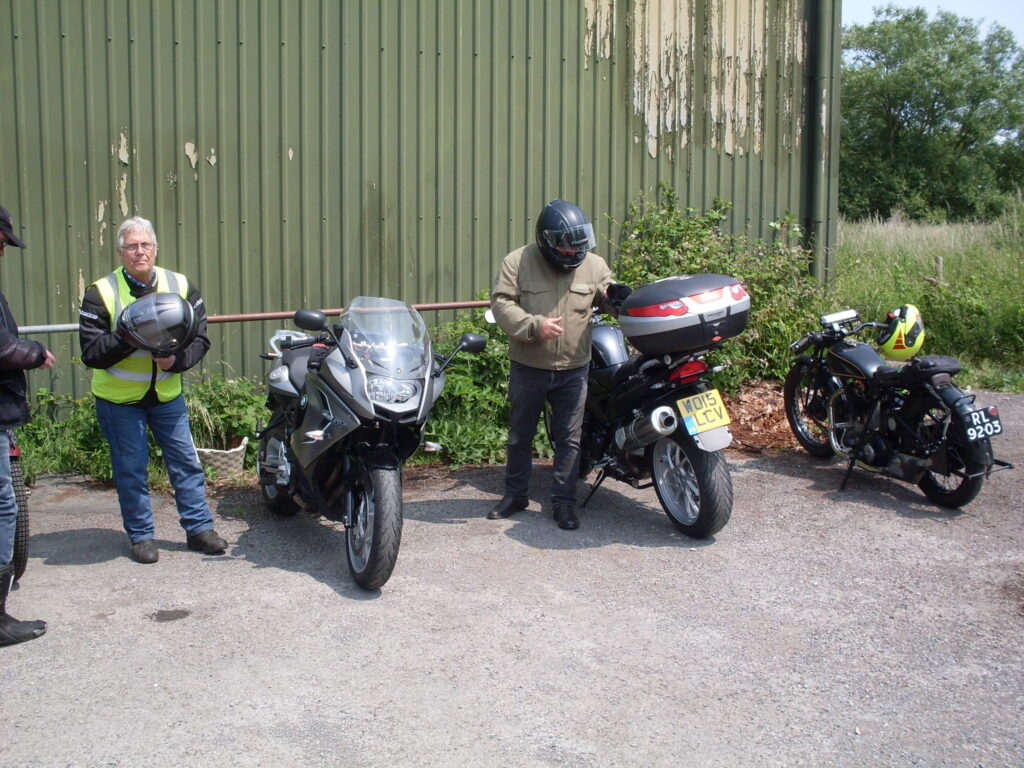 A line of bikes, two are modern BMWs (with riders beside them) and on the end is a much older black Sunbeam motorcycle