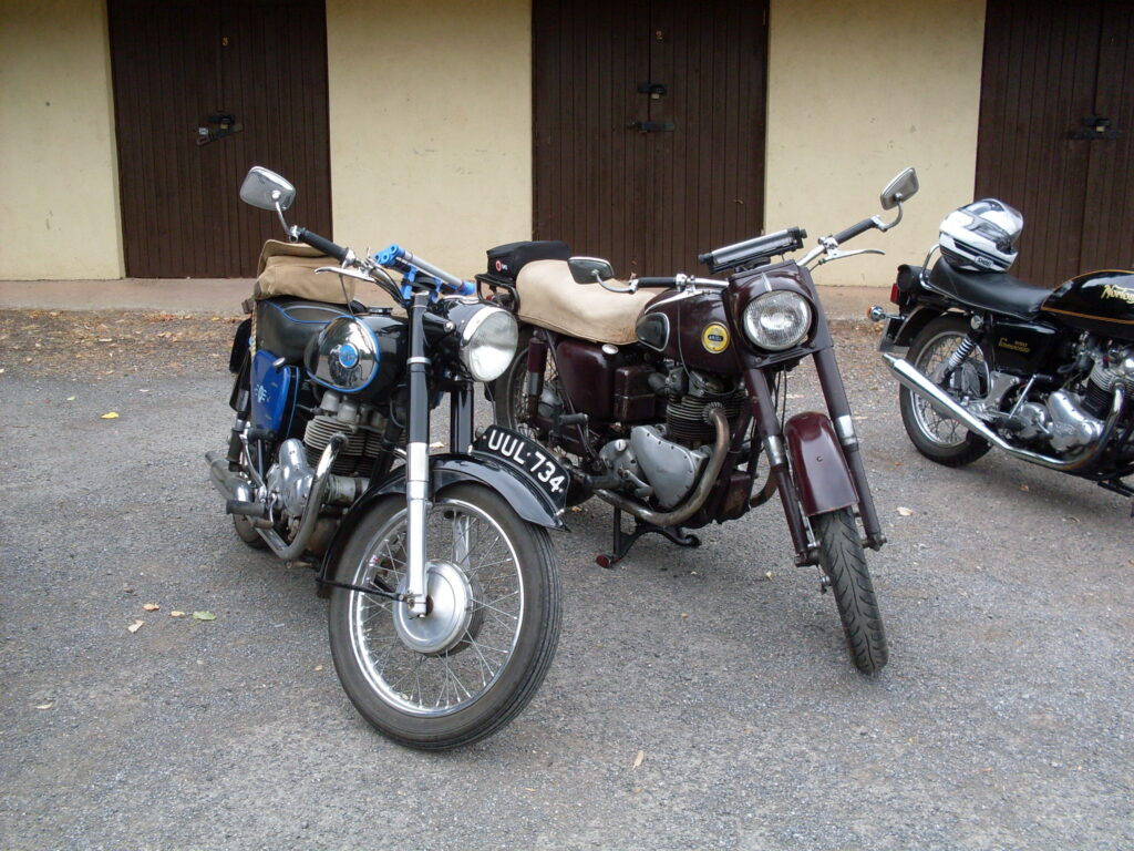 Two motorcycles (one blue, black and chrome, the other very dark red) parked in front of a cream wall with a row of dark brown wooden double doors.