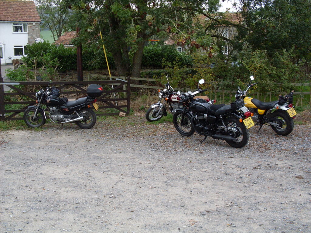 Several relatively modern motorcycles parked with a hedge and trees in the background