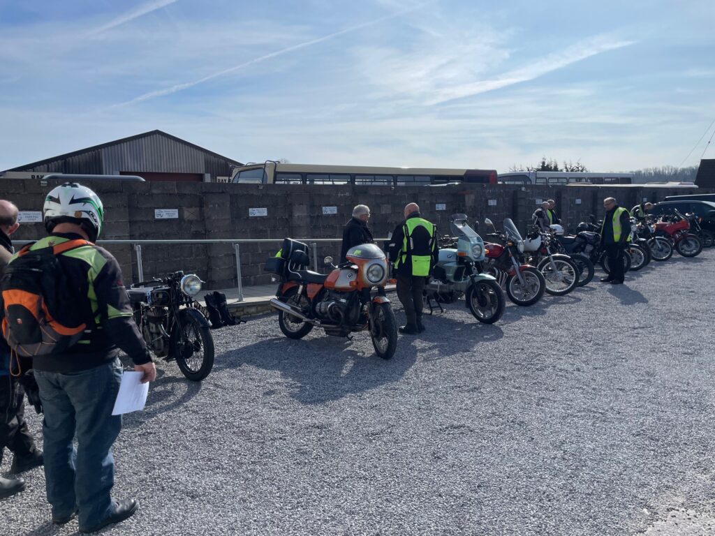 The line of motorcycles but now with a black re-war bike nearest the camera with two people stood looking at it.