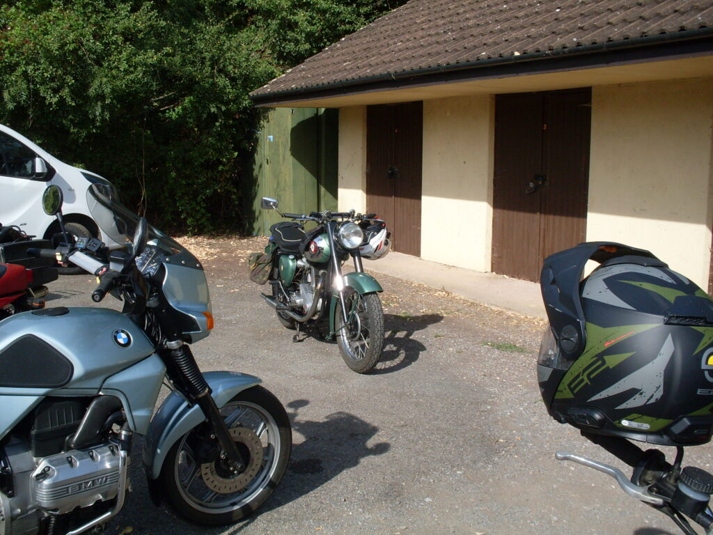 In a gap between other parked machines a green BSA  single-cylinder bike has the sunlight reflecting from its chrome plating.